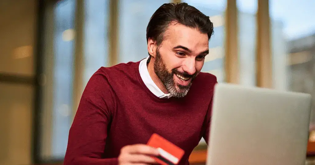 man happily checking his bank balance on a laptop while holding a credit card